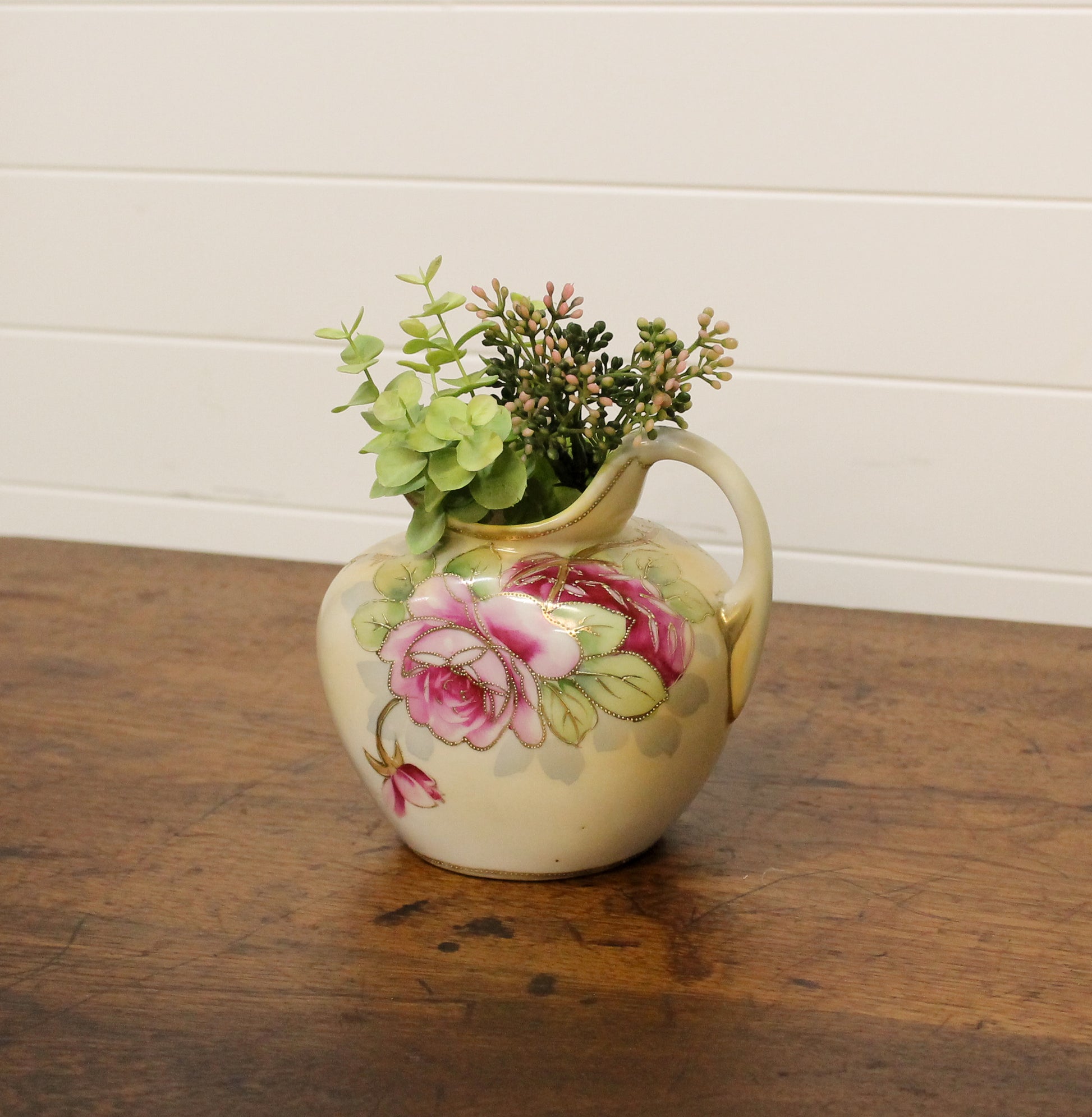 Decorative ceramic pitcher with floral design on a wooden surface