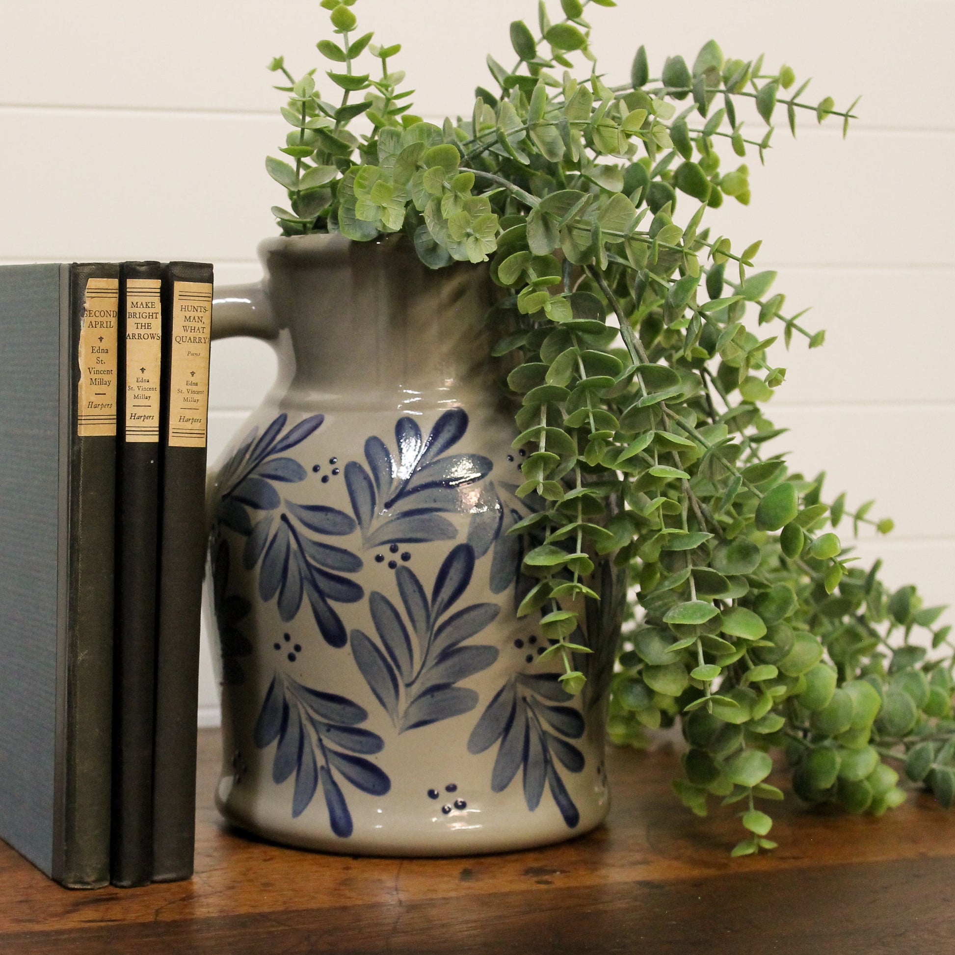 Ceramic pitcher with blue floral patterns holding greenery on a wooden surface.