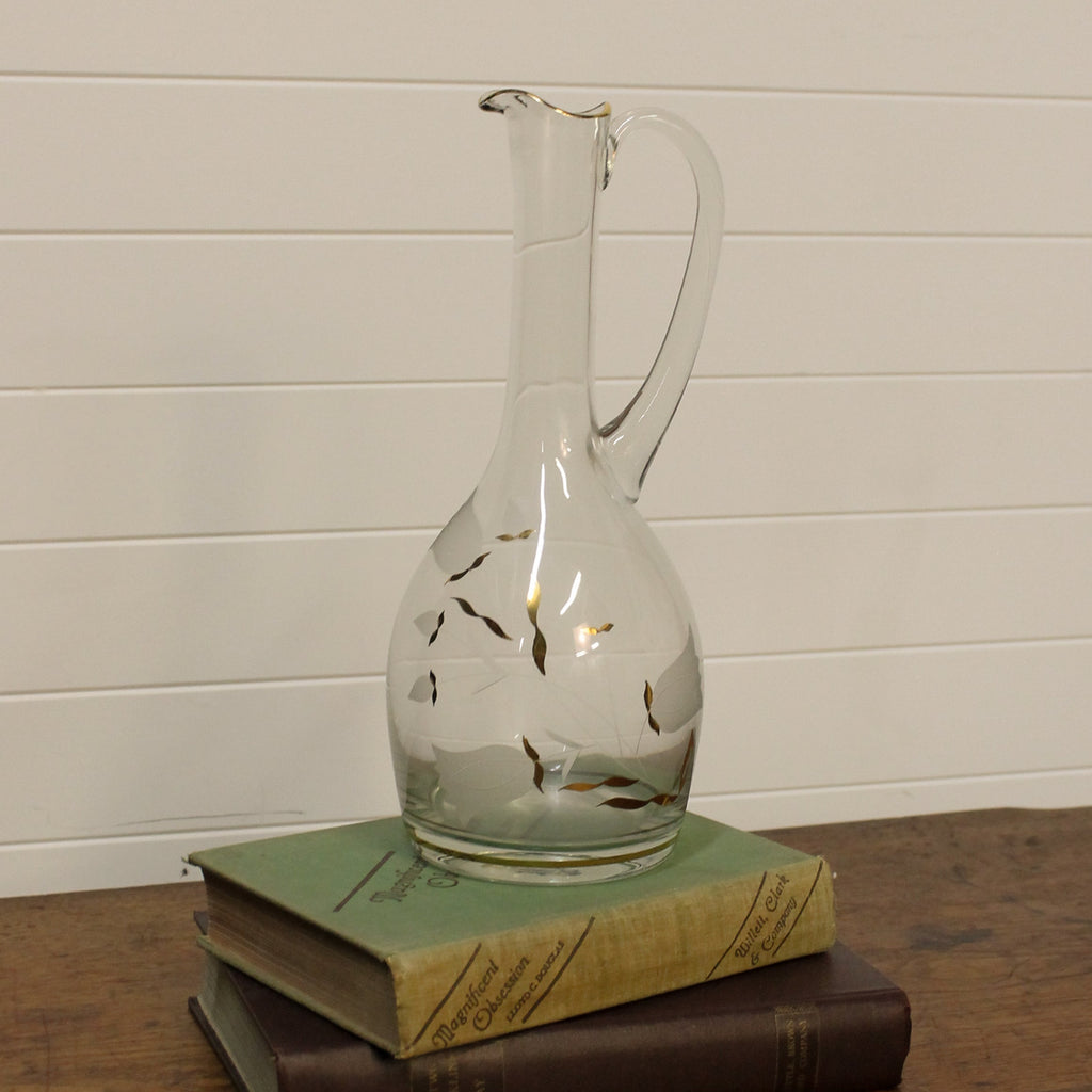 Clear glass decanter with floral design on a stack of books against a white wall.